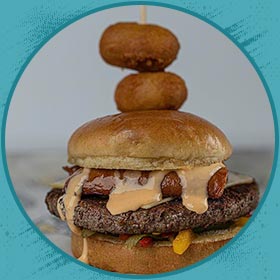 Burger with sauce, sausage, and onion rings—classic Florida burgers against a blue backdrop.