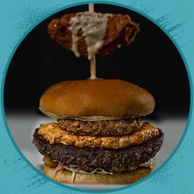 A stacked burger with a fried patty, onion ring, and fried wing—perfect with Florida beer.