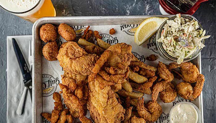 A tray of fried fish, fries, hush puppies, coleslaw, and a lemon wedge with Florida beer nearby.