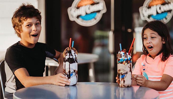 Two excited kids at Gulf Coast Burger Company sit with large, decorated milkshakes before them.