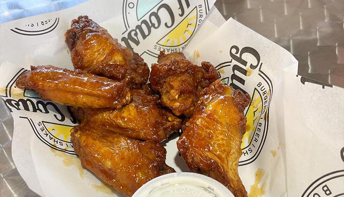 Basket of glazed chicken wings with dipping sauce on Gulf Coast Burger Company branded paper.