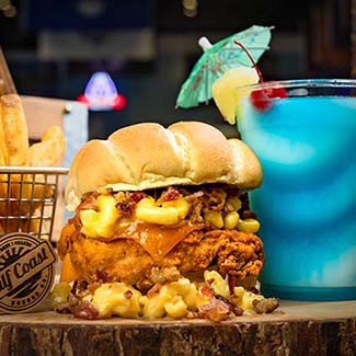 Fried chicken sandwich with mac and cheese, fries, and a Gulf Coast Burger Company tropical drink.