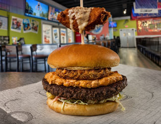 Burger with fried chicken, cheese sauce, onion ring, and lettuce in a Florida restaurant setting.