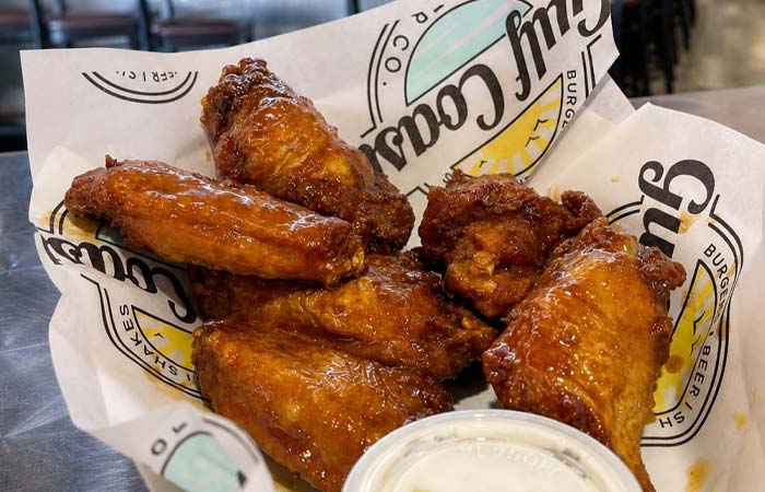 Six saucy chicken wings, served on branded paper at Gulf Coast Burger Company, with ranch sauce.