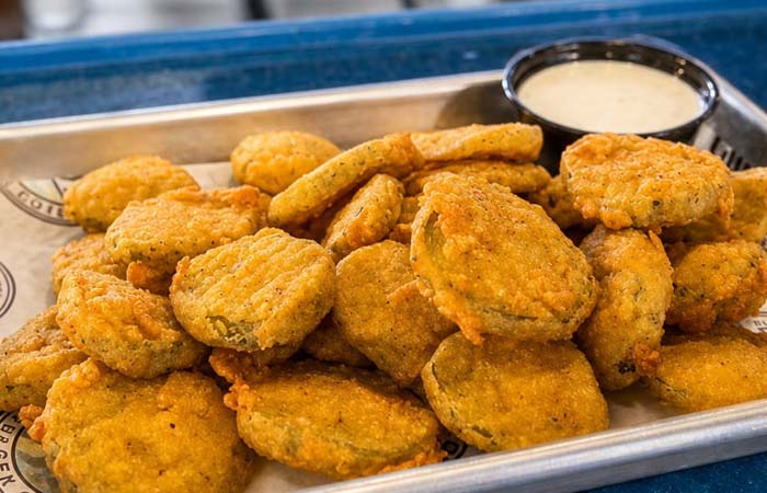 Fried pickle slices on a tray at Gulf Coast Burger Company, served with white dipping sauce.