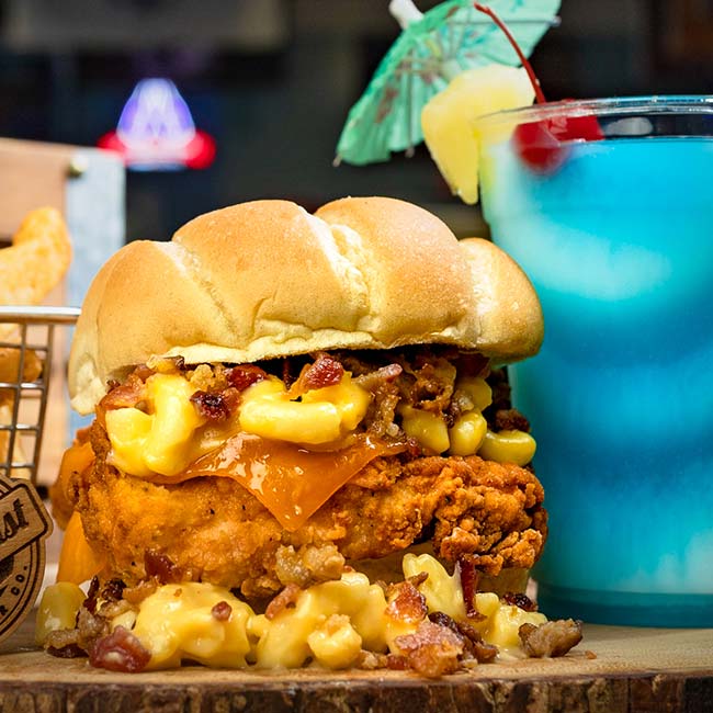 Fried chicken sandwich with macaroni, bacon, cheese at our restaurant; blue frozen fruit drink.