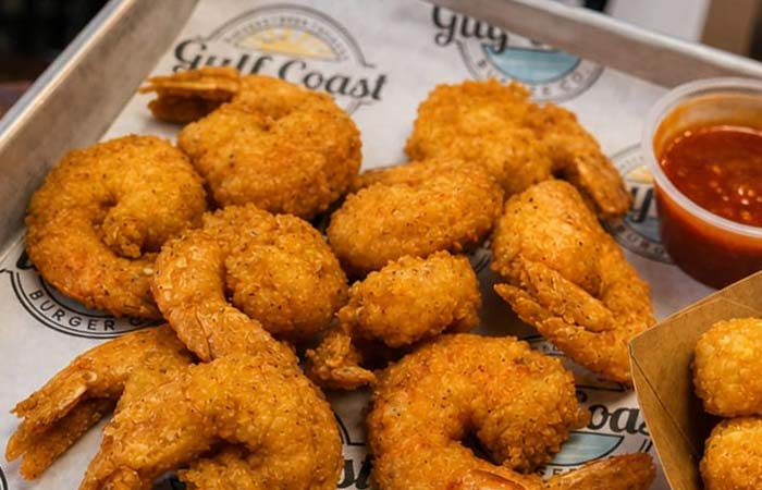 Fried shrimp on a tray with cocktail sauce, perfect alongside our burgers or classic shakes.