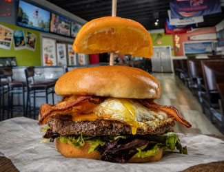 Burger with lettuce, bacon, fried egg, and orange slice at Gulf Coast Burger Company diner.