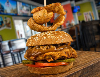 Fried chicken sandwich with pickles, tomato, sauce, and onion rings at Gulf Coast Burger Company.